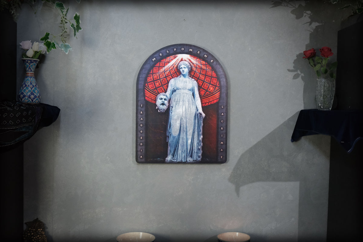 A gothic-style wall plaque featuring a statue of a woman holding a skull, set against a red patterned background, mounted on a textured gray wall with decorative vases on either side. dark academia decor Melpomene
Muse of Tragedy