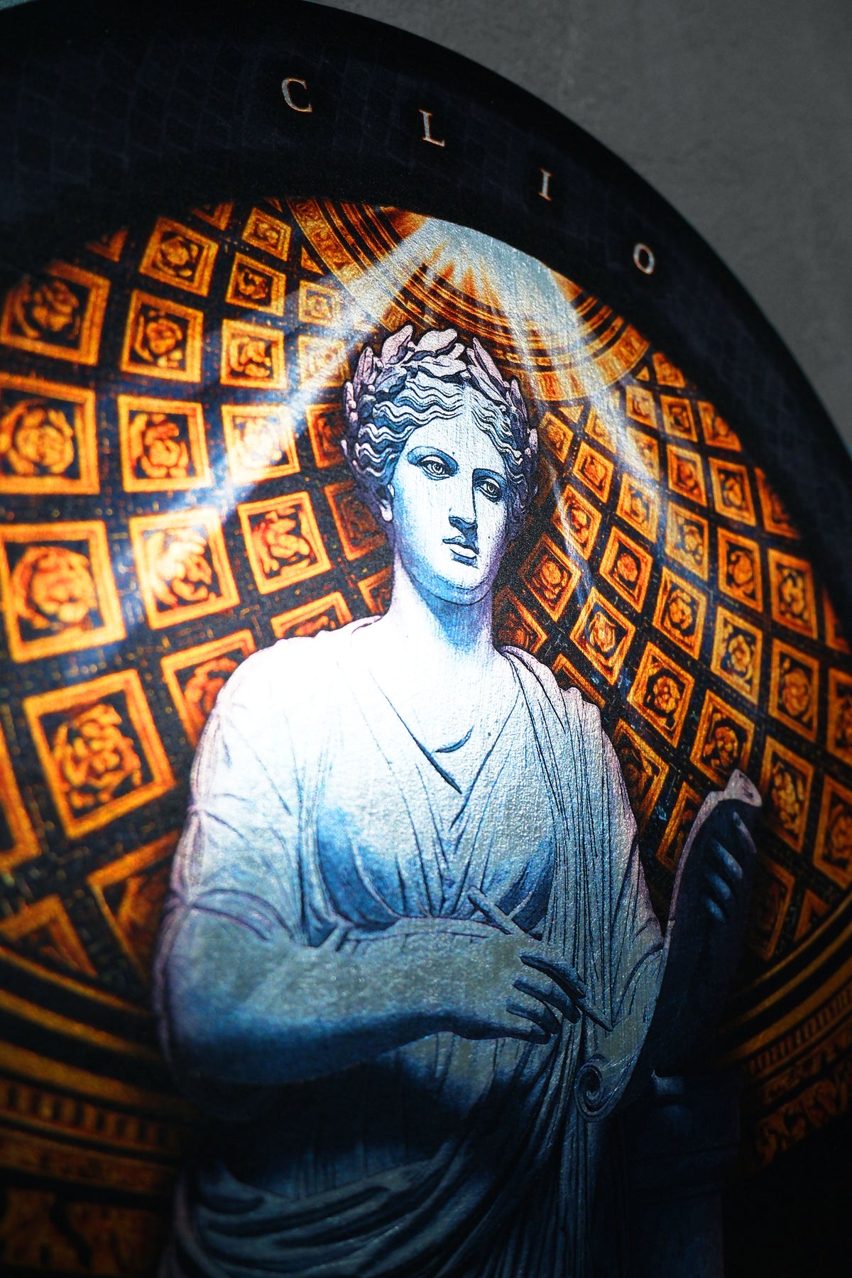 Close-up of a circular decorative plaque or wall art featuring a classical draped figure in blue-gray tones against an orange and black patterned background with a glowing halo effect. dark academia decor Clio — Muse of History