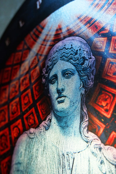 A close-up of a circular decorative plate or coaster featuring a stylized classical female bust in pale blue-gray tones against a red and black geometric  dark academia decor  Melpomene
Muse of Tragedy