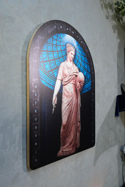 An arched decorative wall plaque featuring a classical statue illustration of Urania with a blue patterned background and the words 'URANIA ASTRONOMIA' on a textured light gray wall.  Urania is the Greek Muse of astronomy and astrology