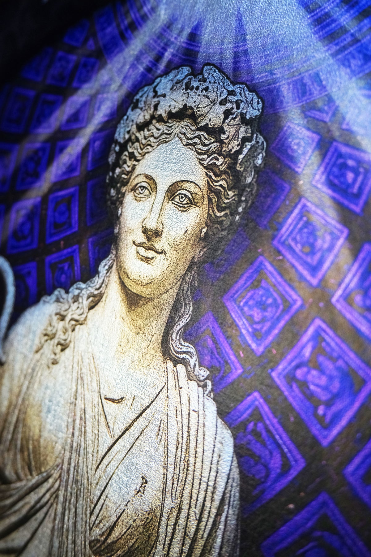 A close-up of a classical bust sculpture in light beige stone, set against a dark background with glowing blue and purple geometric patterns and light rays. Thalia. Muse of Comedy