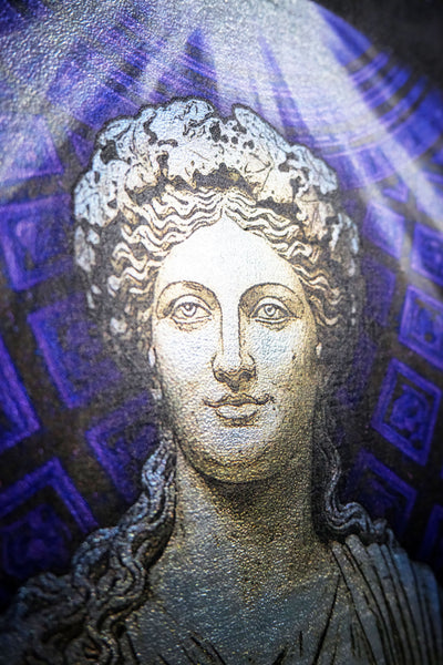A close-up of a textured mosaic or print depicting a classical female bust with curly hair, rendered in gray and white tones against a purple and blue patterned background. Thalia. Muse of Comedy