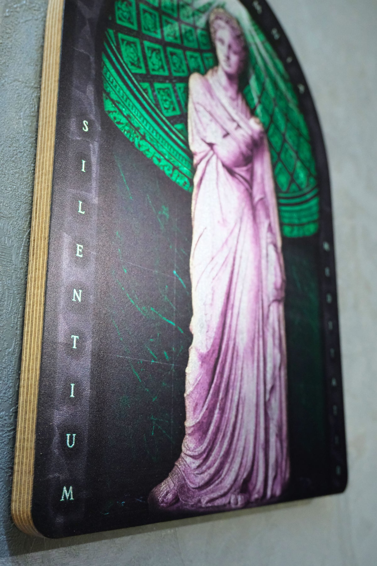 A rectangular wall art print or plaque with rounded top corners, featuring a pale pink draped female statue against a dark background with green geometric patterning and the word 'SILENTIUM' running vertically along the left edge. Polyminia is a common alternative spelling of Polyhymnia (or Polymnia), the Greek Muse of sacred poetry, hymns
