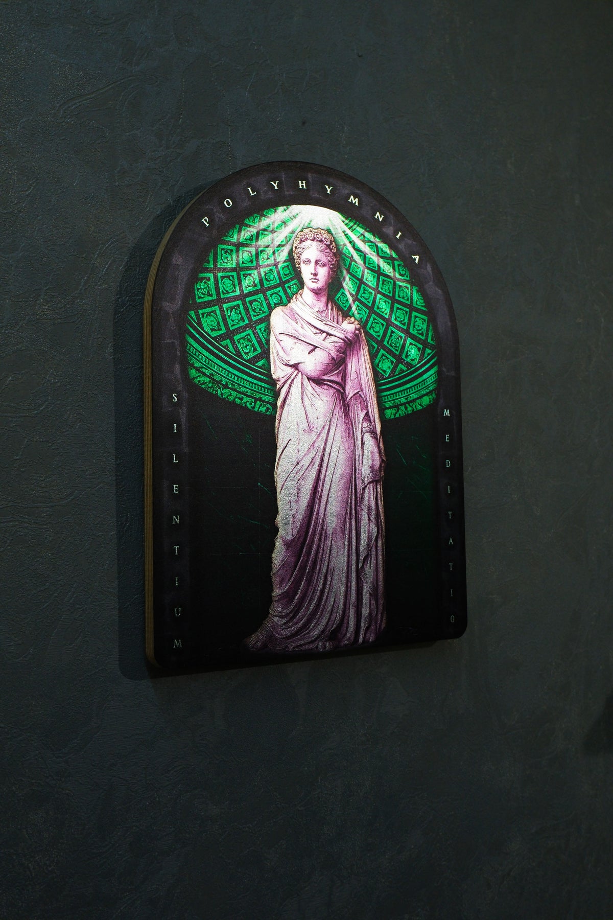 An arched decorative wall plaque featuring a classical statue of a draped female figure, set against a glowing green geometric pattern on a dark background, mounted on a textured dark gray wall. Polyminia is a common alternative spelling of Polyhymnia (or Polymnia), the Greek Muse of sacred poetry, hymns