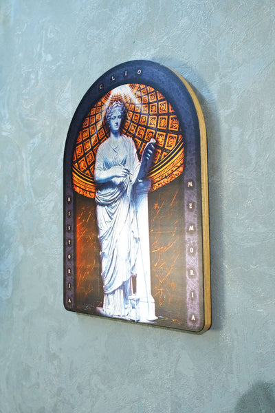 An arched religious wall plaque depicting the Virgin Mary in a white robe against an orange and gold patterned background, mounted on a textured light blue-gray wall. dark academia decor  Clio — Muse of History