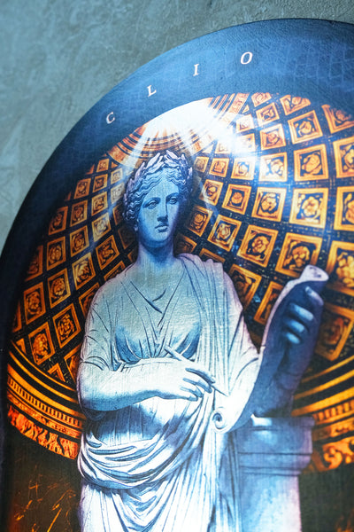 A close-up of a circular decorative print or tile featuring a classical statue of a draped female figure in white, set against a gold and black patterned background with the word 'CLIO' at the top. dark academia decor  Clio — Muse of History