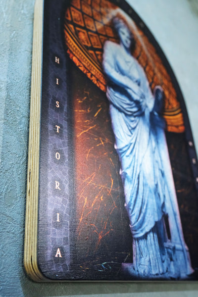 A close-up of a printed card or book page featuring a classical statue in blue-gray tones against an orange-brown arch, with the word 'HISTORIA' printed vertically on the left side. dark academia decor  Clio — Muse of History