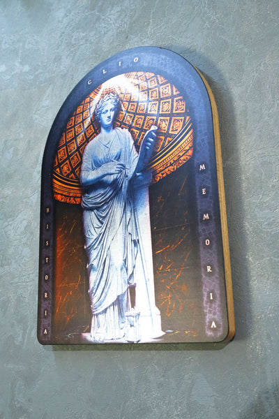 An arched decorative plaque featuring a blue-toned statue of a robed figure holding a book, with orange geometric patterns in the background and vertical text reading 'historia' on the left and 'MEMORIA' on the right, mounted against a textured gray wall. dark academia decor  Clio — Muse of History